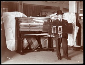 A Piano by Ricca und Son Piano Co. with a Man Adjacent Holding Up Part of the Piano Works by Byron Company